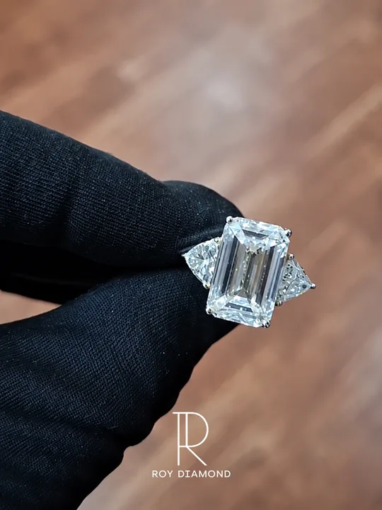 Emerald-cut centre diamond ring with triangular side stones held in a black glove